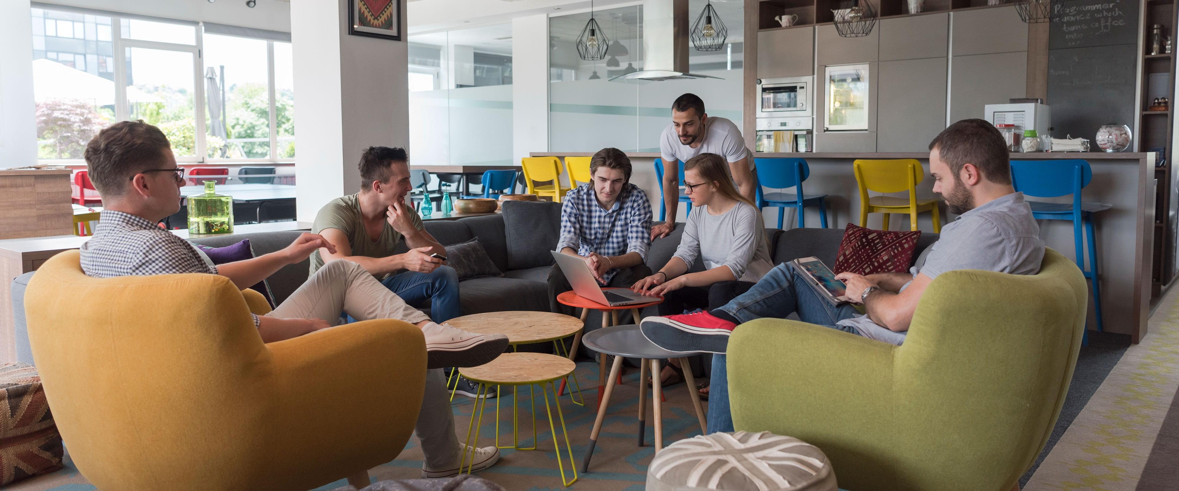 Besprechung einer Gruppe von sechs Personen, sitzend auf Sofa und Sesseln in moderner und gemütlicher Büro-Umgebung
